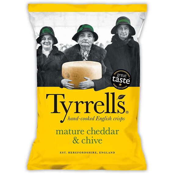 Tři ženy v kloboucích, prostřední drží velký bochník sýra, pod nimi nápis Tyrrells  bramborové chipsy hand-cooked English crisps s příchutí zralý čedar a pažitka. Hmotnost 150 g